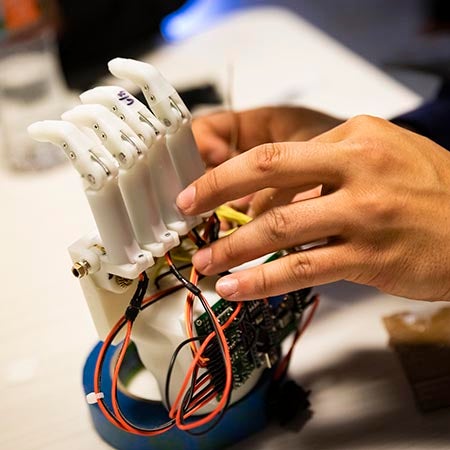 Close-up of a person's hands as they work on a robotic hand model.