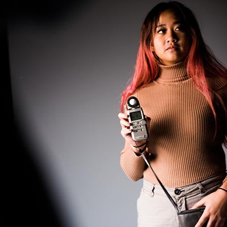Portrait of a woman looking off into the distance in a photography studio holding a light sensor.