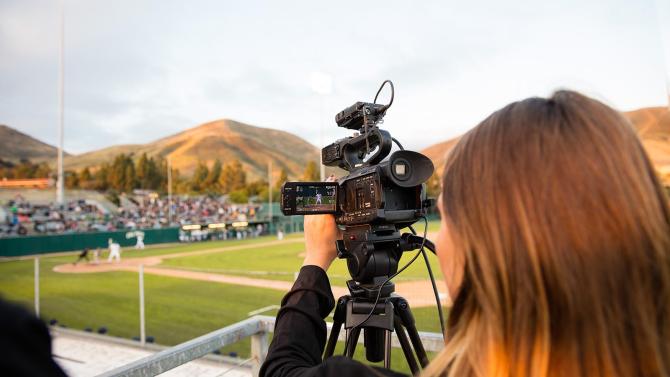 A woman aims a video camera at a baseball game.